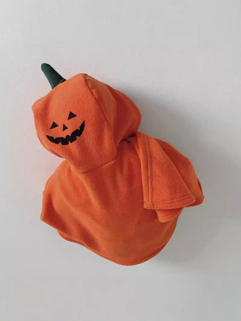 An orange hooded plush toy or costume accessory shaped like a pumpkin, with a black embroidered jack-o'-lantern face and a dark green stem, photographed against a plain light background.