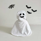 White ghost costume with black face design on a light gray background with Halloween decorations.