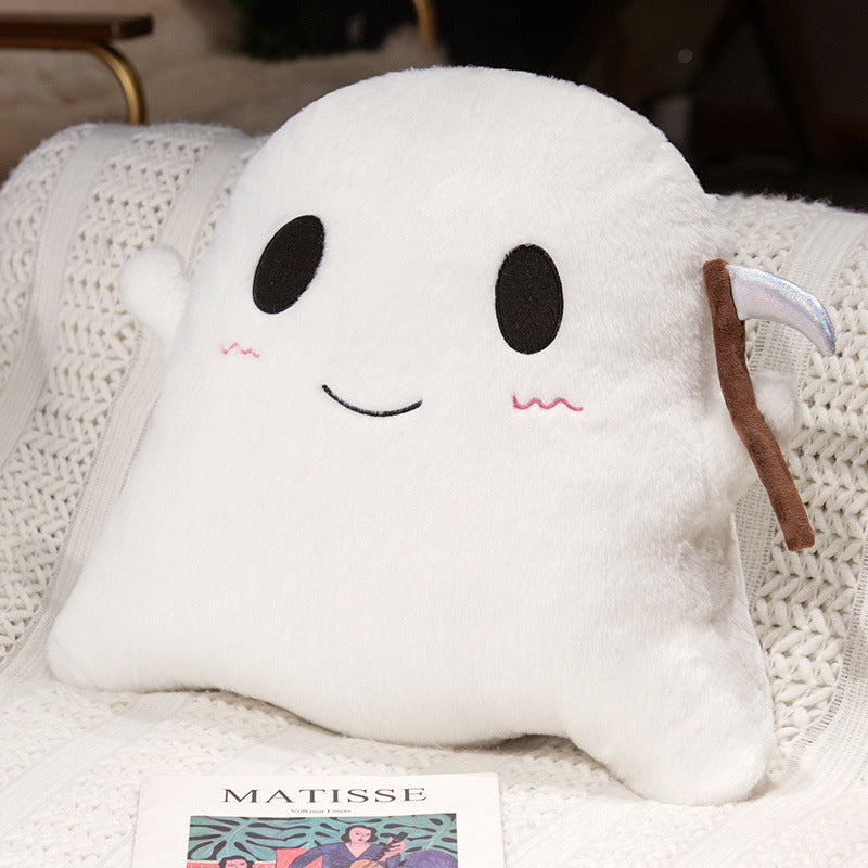 A white plush ghost-shaped pillow with embroidered black eyes and mouth, pink cheek details, and a brown scythe accessory, resting on a white knitted blanket.