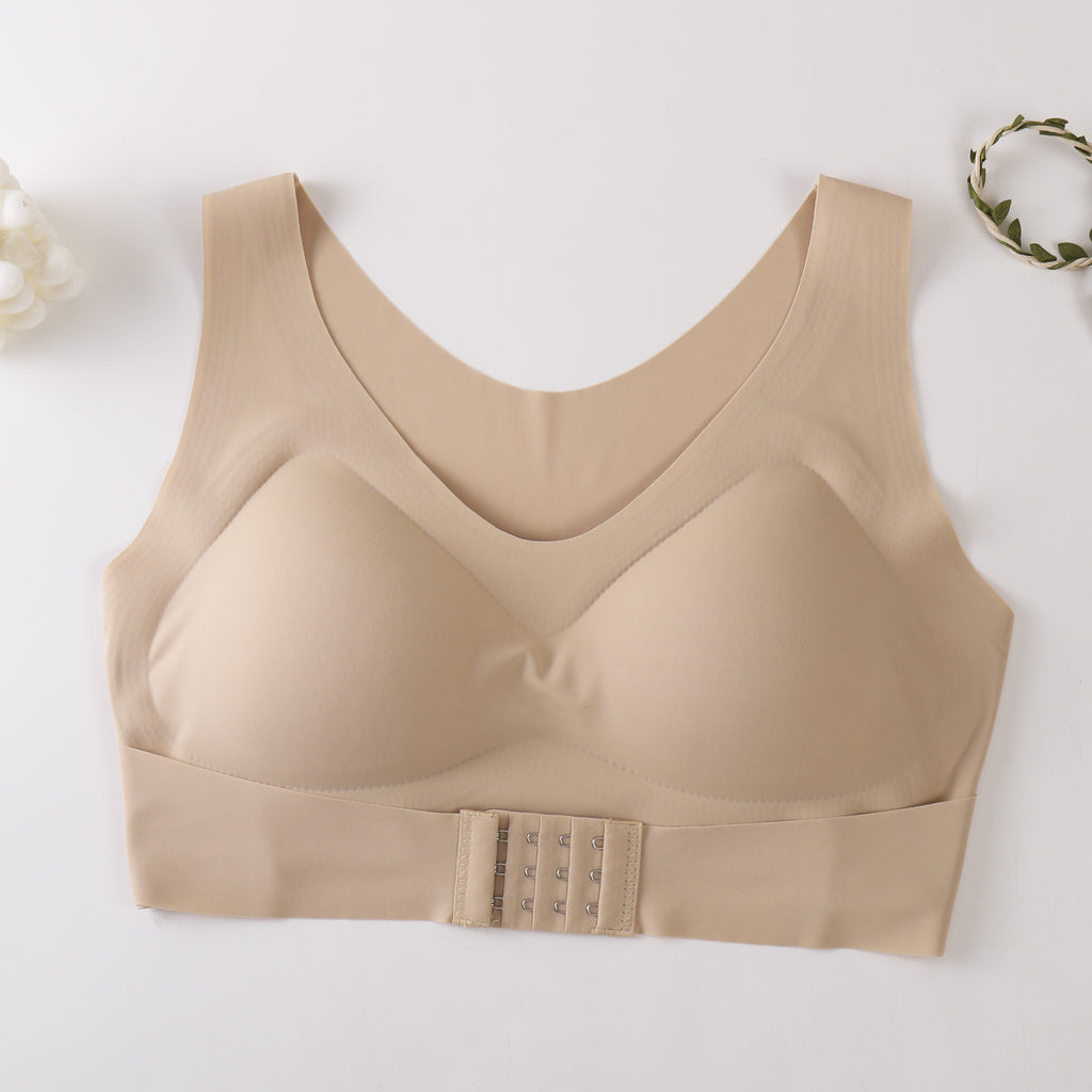 A beige wireless bra with a wide underband and a central triple-hook closure, laid flat on a light background with small decorative floral props in the corners.
