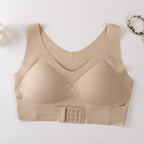 A beige wireless bra with a wide underband and a central triple-hook closure, laid flat on a light background with small decorative floral props in the corners.