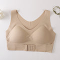 A beige wireless bra with a wide underband and a central triple-hook closure, laid flat on a light background with small decorative floral props in the corners.