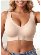 A woman wearing a light beige wireless bra with a wide underband and a central double-gauge closure, paired with blue jeans.