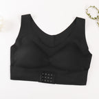 A black wireless bralette with a wide underband and a three-hook closure strap, laid flat on a white background with a decorative leafy vine in the top right corner.