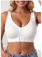 A woman wearing a white wireless bralette with a wide underband and a central adjustable hook-and-eye closure, paired with blue jeans.