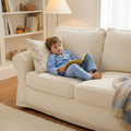 A boy is wearing the cotton pajamas with long pants long sleeves and reading a book on a sofa.