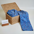 A blue cotton pajama set with a sailboat pattern, folded inside and draped over an open wicker chest.