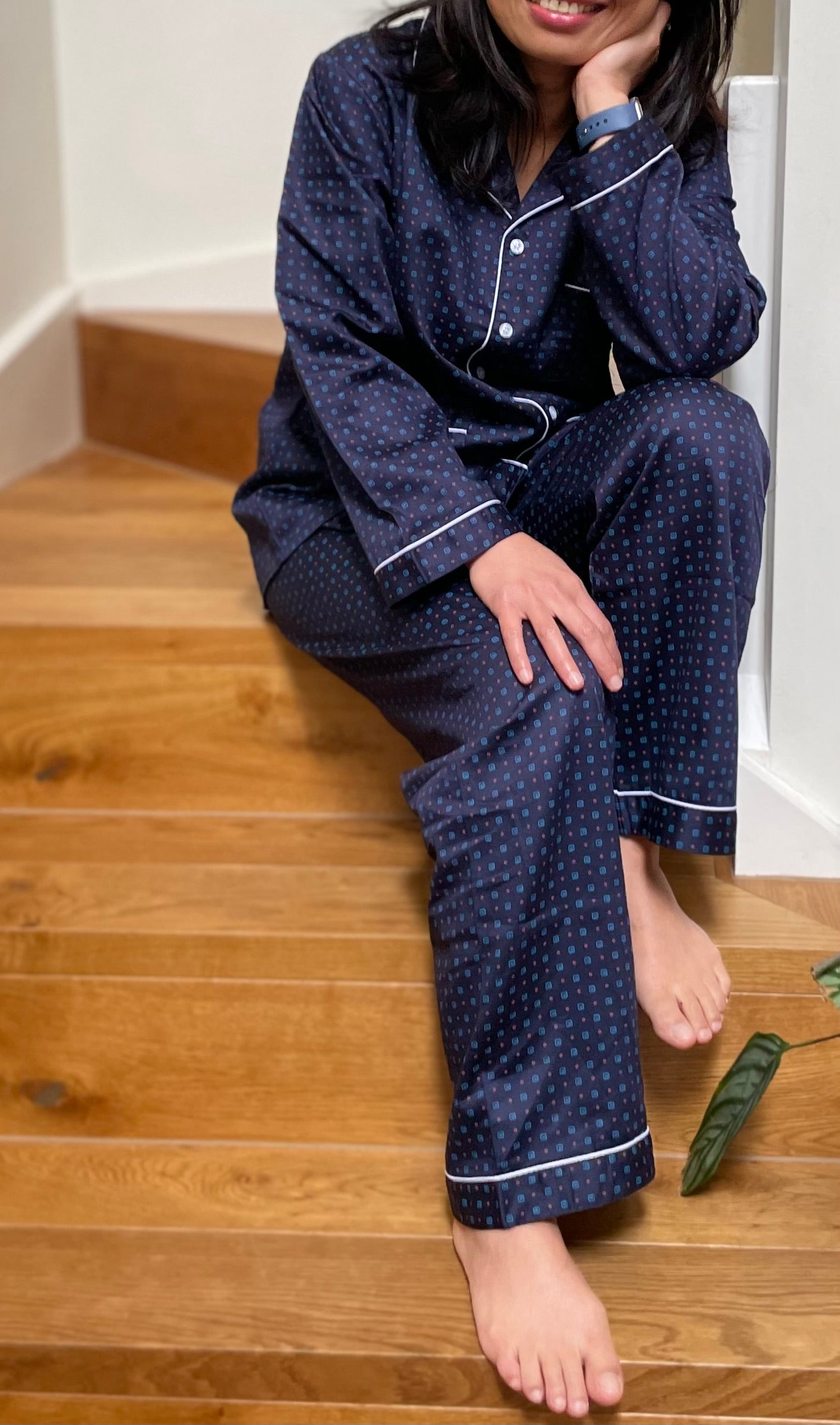 Person wearing navy blue polka dot pajamas sitting on a wooden floor.