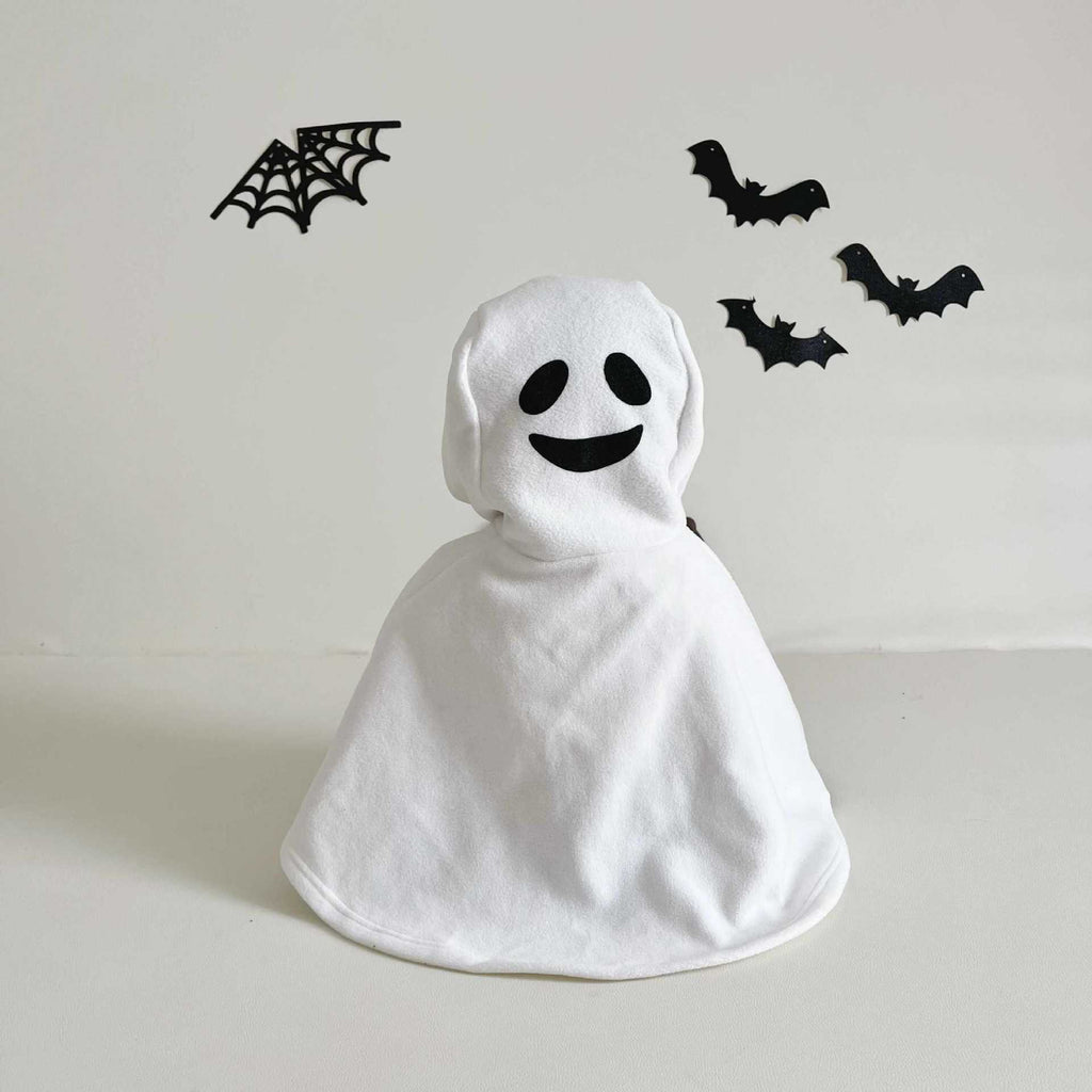 White ghost costume with black face design on a light gray background with Halloween decorations.