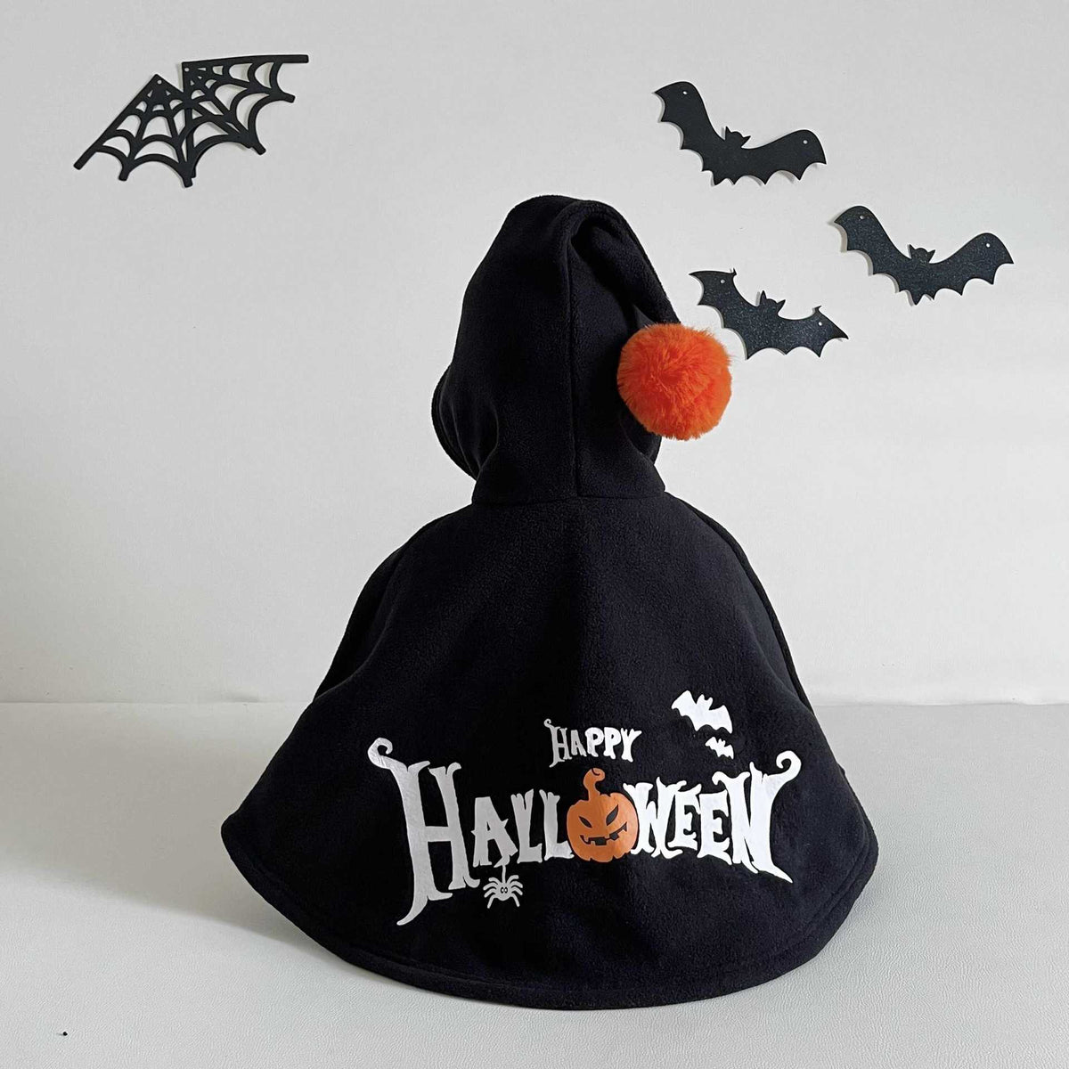 Black Halloween cape with pom-pom and 'Happy Halloween' text on a white background