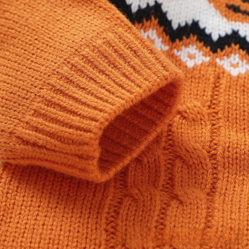 Close-up of a textured knit sweater in burnt orange, showing a ribbed cuff and cable-knit pattern, with a partial view of a black, white, and orange patterned section.